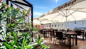 An outdoor seating area with tables and chairs under large umbrellas with the brand 'Tucher' visible. - Hotel Randsbergerhof (Cham)