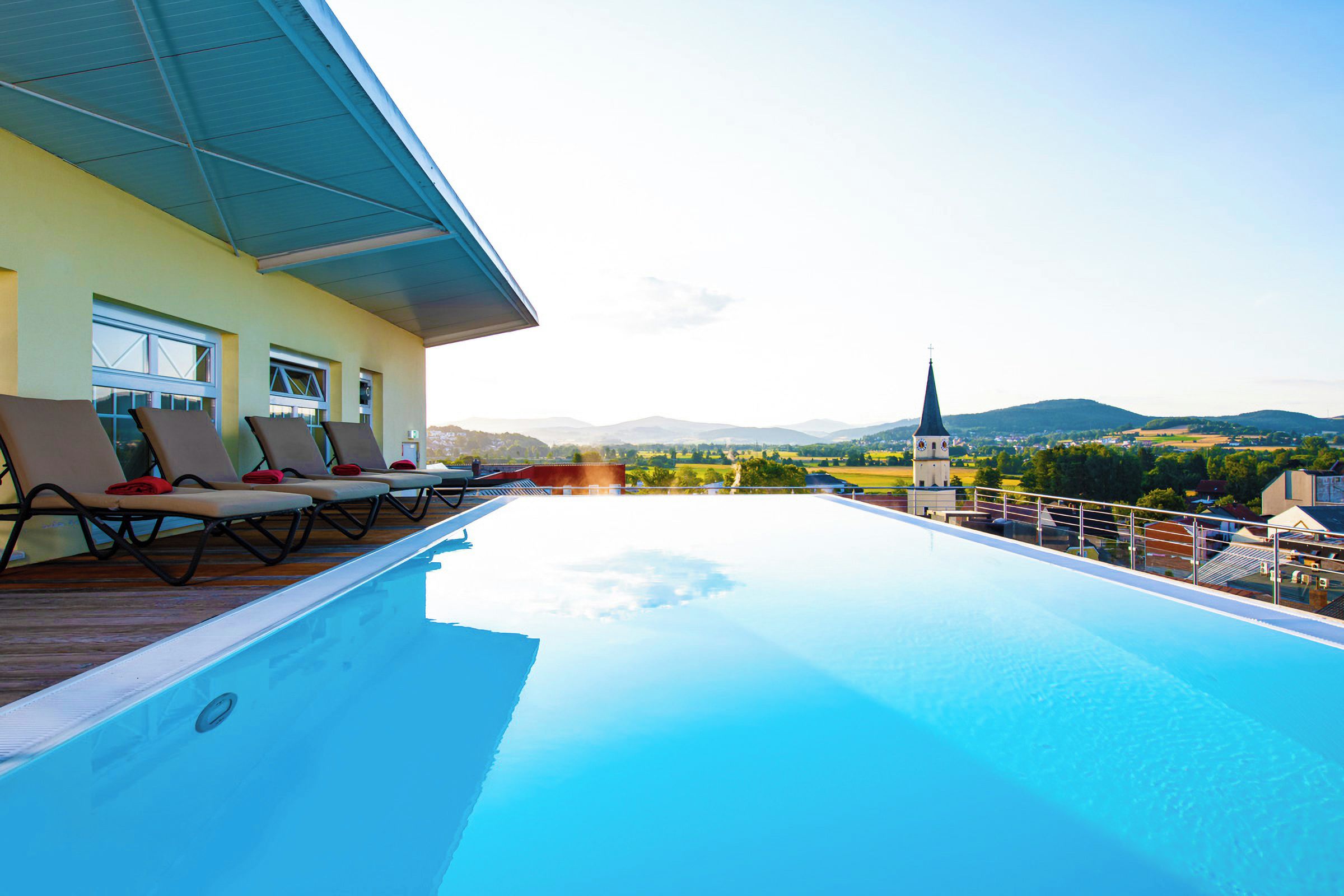 Ein Pool auf dem Dach mit Liegestühlen, Blick auf die Landschaft und ein Kirchturm in der Ferne.