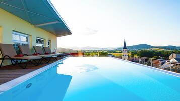 Ein Pool auf dem Dach mit Liegestühlen, Blick auf die Landschaft und ein Kirchturm in der Ferne.