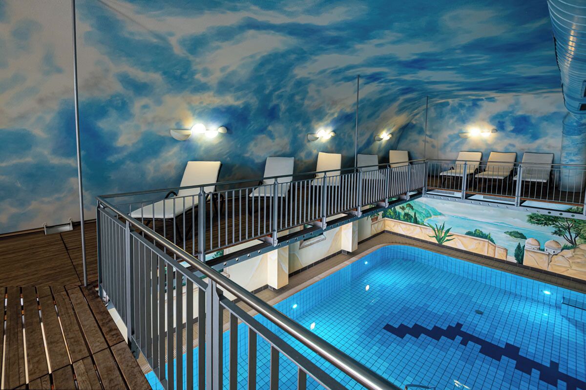 An indoor swimming pool with a wooden deck and a sky mural on the walls.