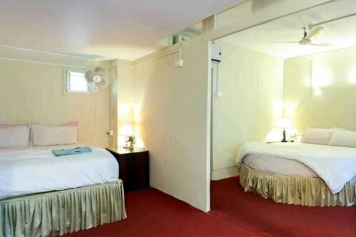 Een hotelkamer met twee bedden, een rood tapijt, een plafondventilator en een raam.