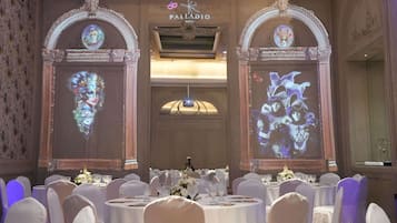 Un salón de banquetes con mesas redondas, sillas blancas y centros de mesa florales.