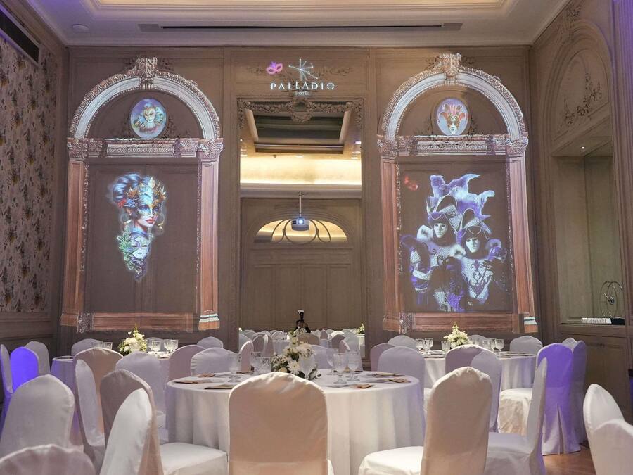 Un salón de banquetes con mesas redondas, sillas blancas y centros de mesa florales.