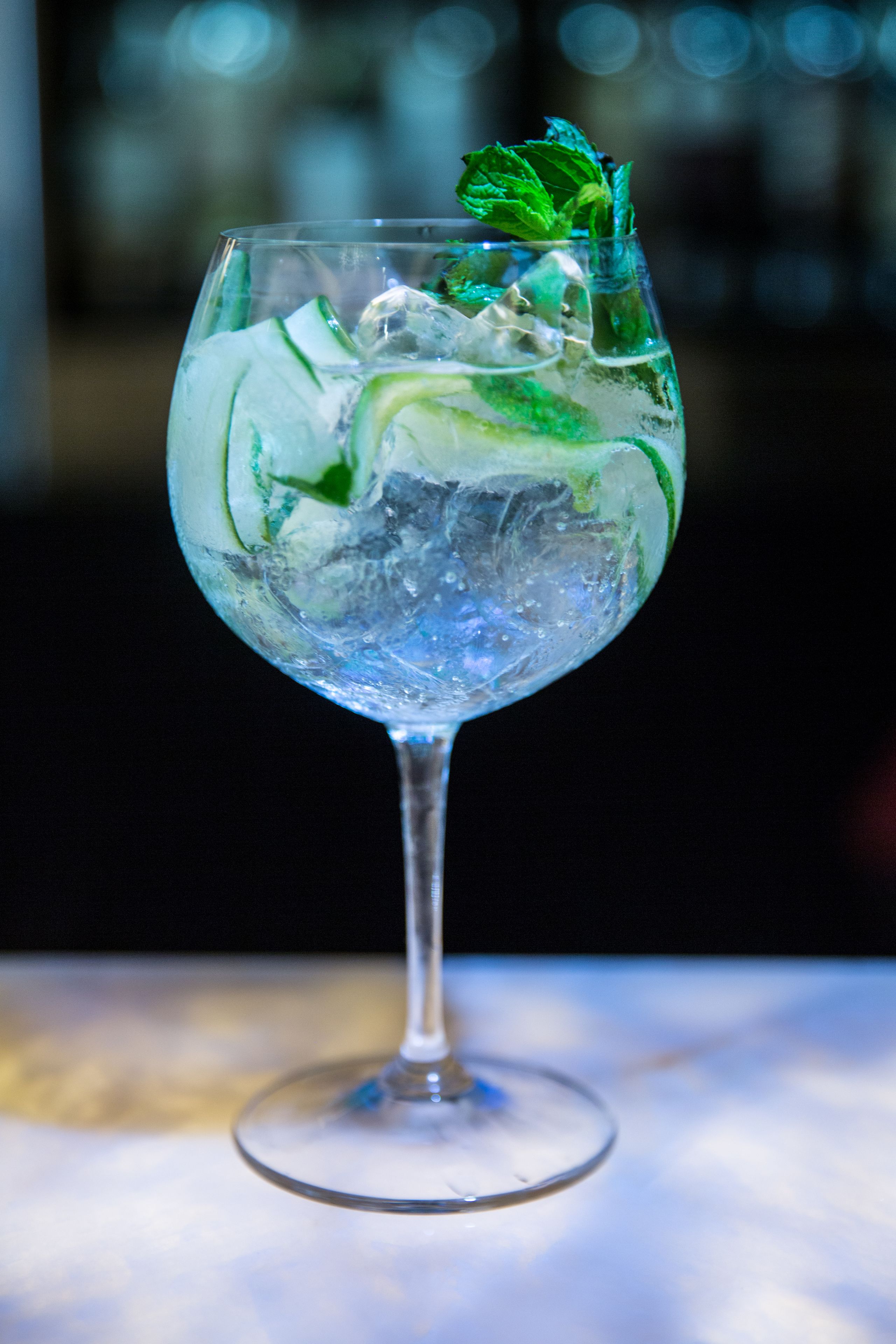 A clear glass with ice cubes and mint leaves, likely a cocktail, on a reflective surface.