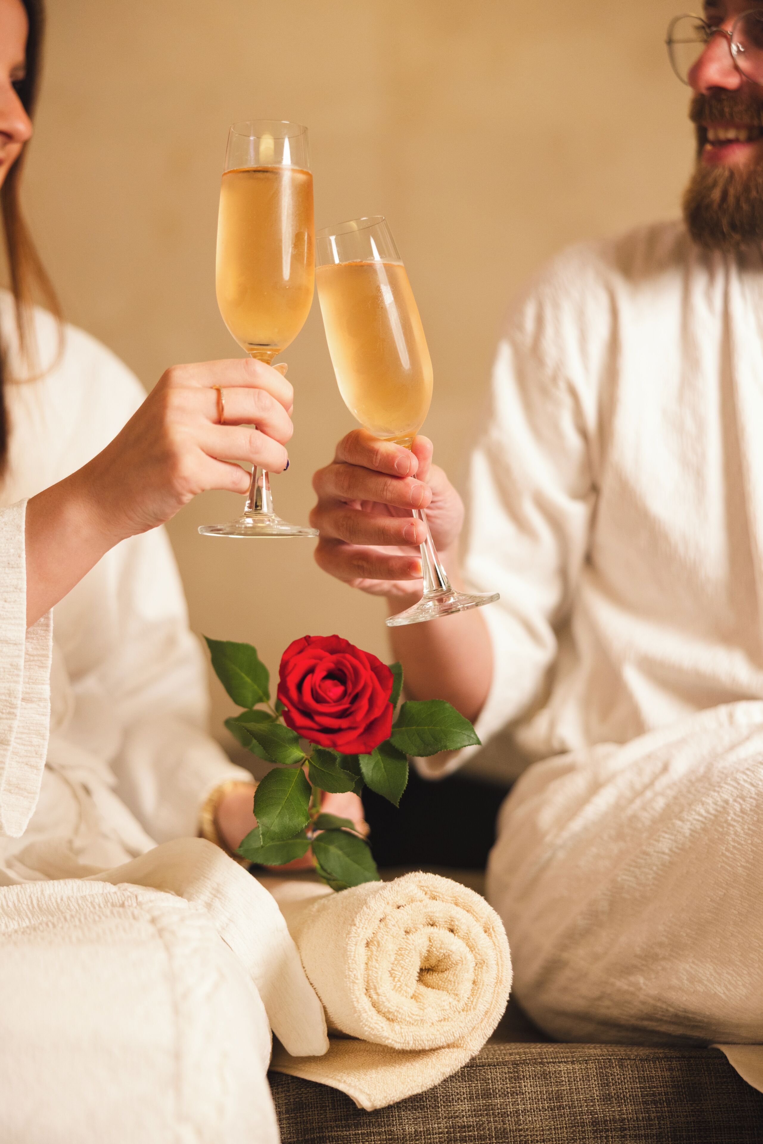 Deux personnes tenant des coupes de champagne, une rose rouge et une serviette enroulée.