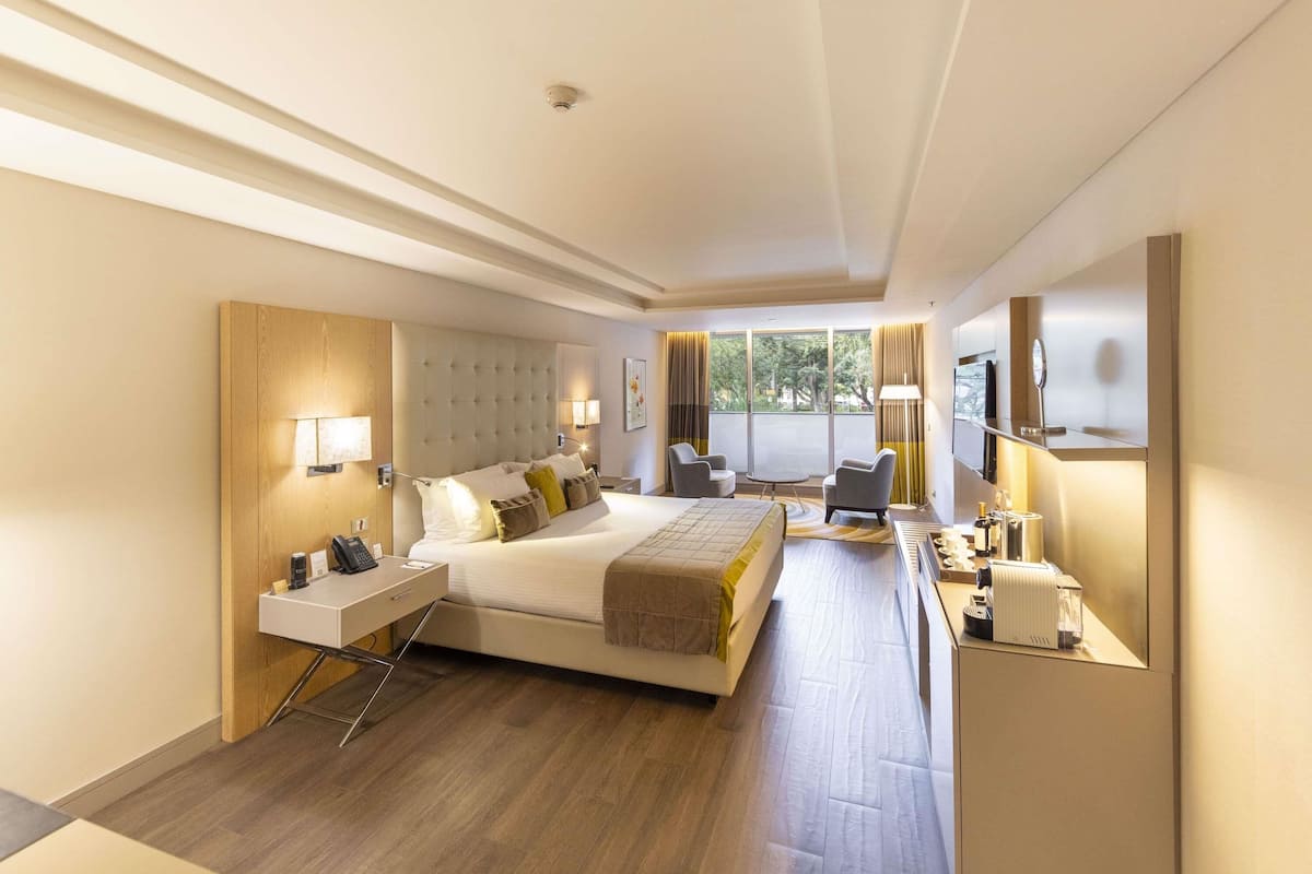 Een moderne hotelkamer met een groot bed, nachtkastjes, een bureau, een stoel, een televisie en uitzicht op het omliggende landschap.