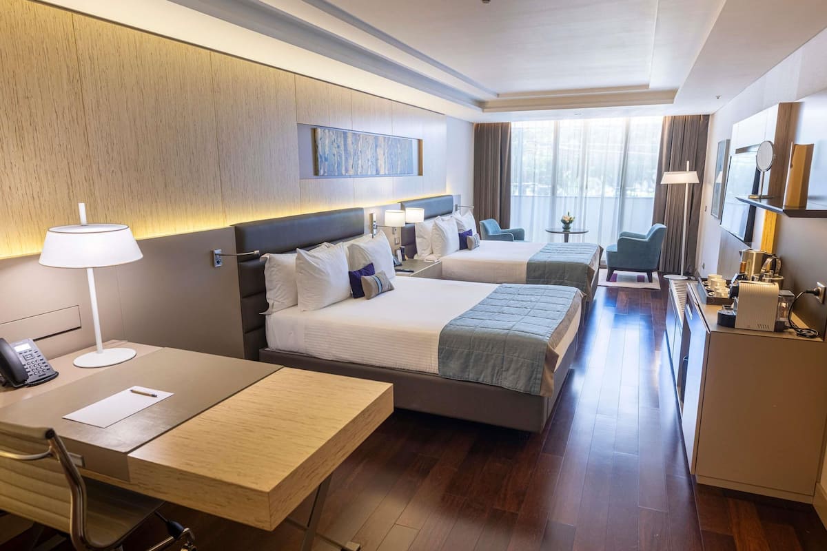 Hotelkamer met twee bedden, een bureau, een stoel, een klein tafeltje, een lamp, een telefoon, een televisie en een koffiezetapparaat.