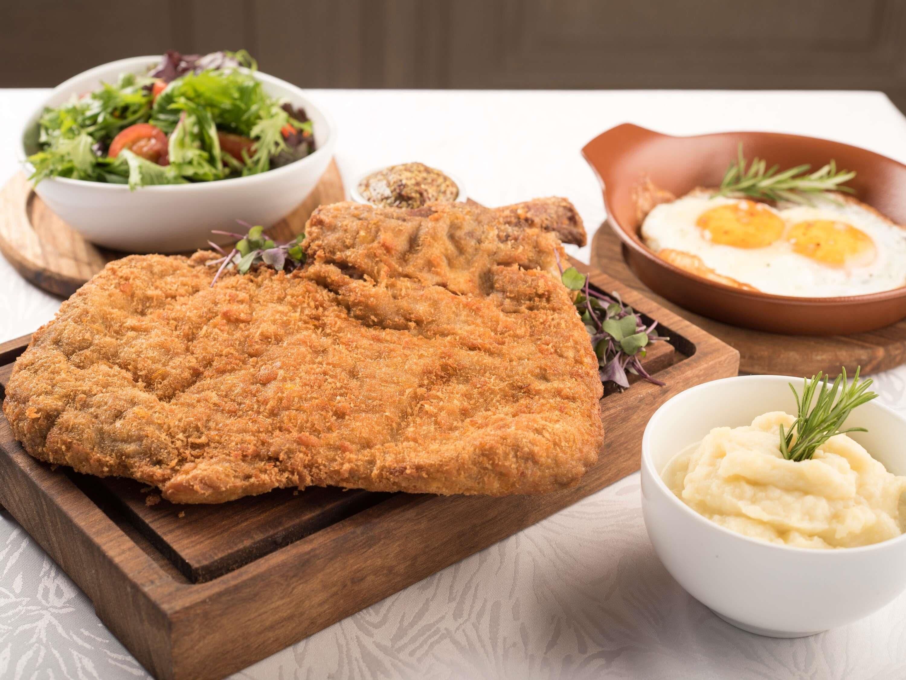 Plato con pescado empanizado, ensalada, puré de papas y huevos fritos.