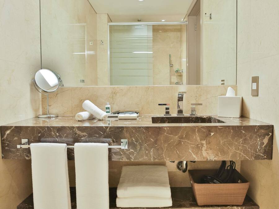 Uma casa de banho moderna com toucador de mármore, um espelho grande, duas toalhas, um dispensador de sabonete e uma caixa de lenços.