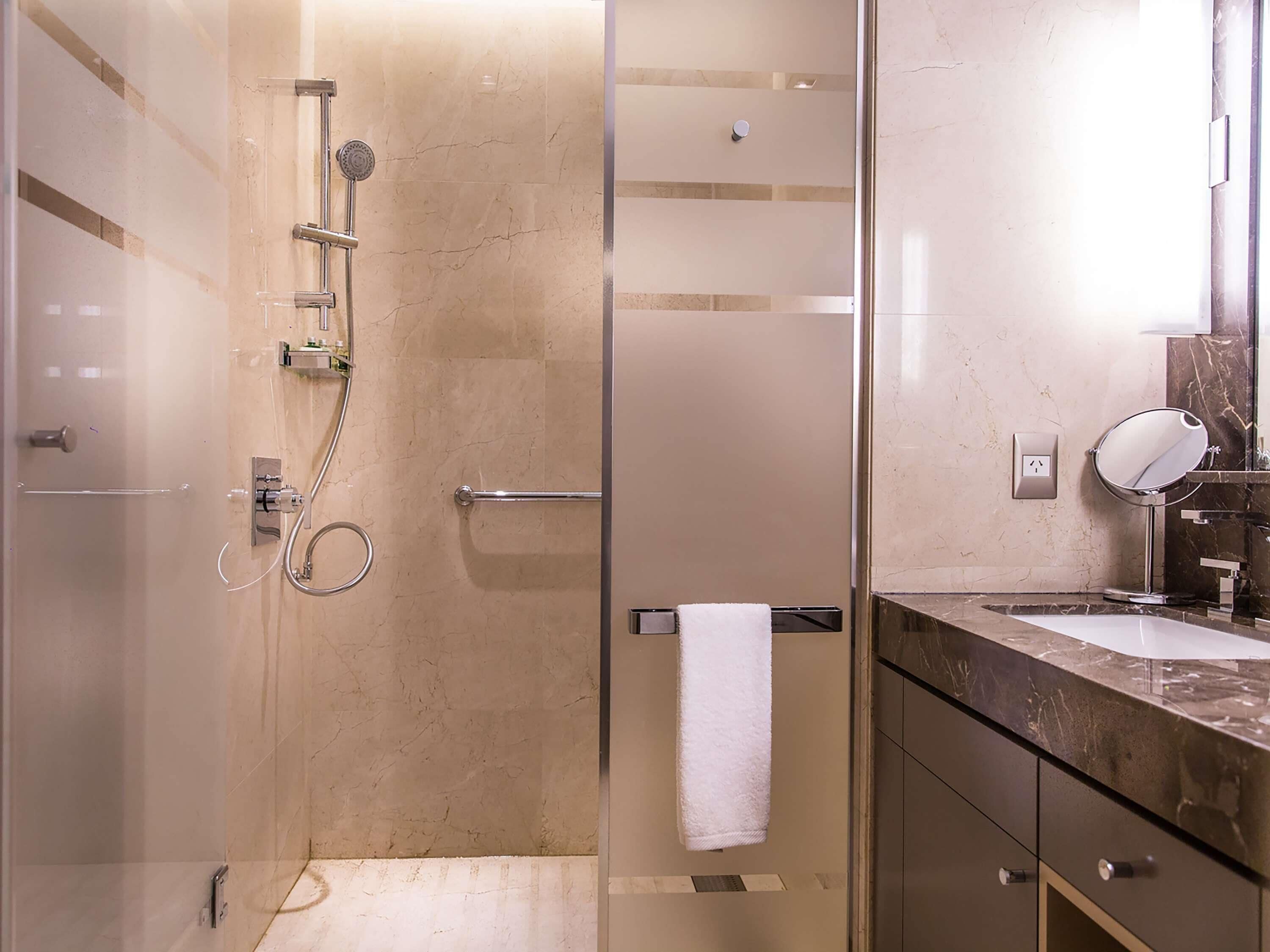 Une salle de bain moderne avec une douche à parois de verre, un mur recouvert de carreaux de marbre, un meuble-lavabo et une serviette suspendue à un porte-serviettes.