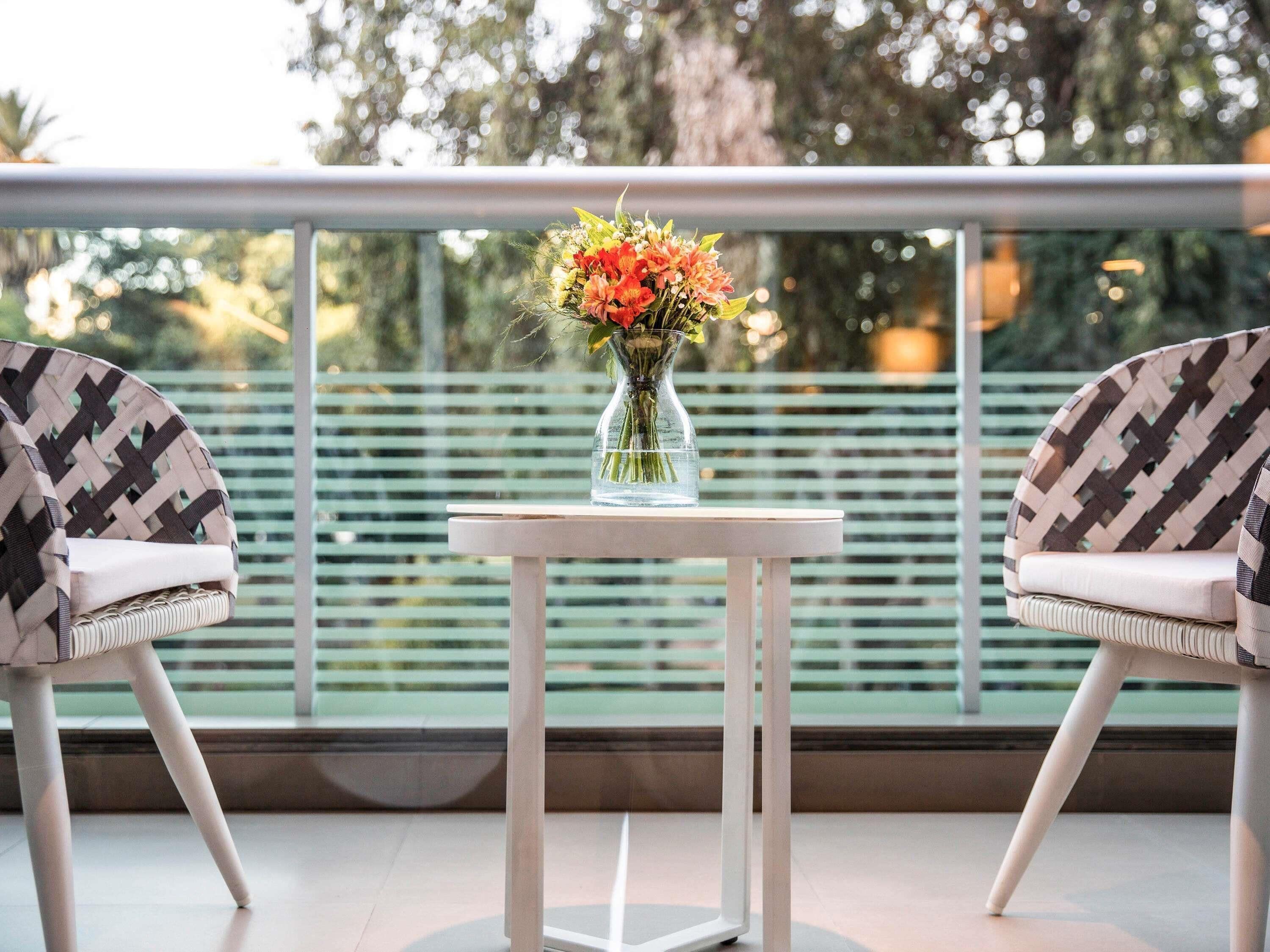 A balcony with two chairs, a small table, and a vase with flowers.
