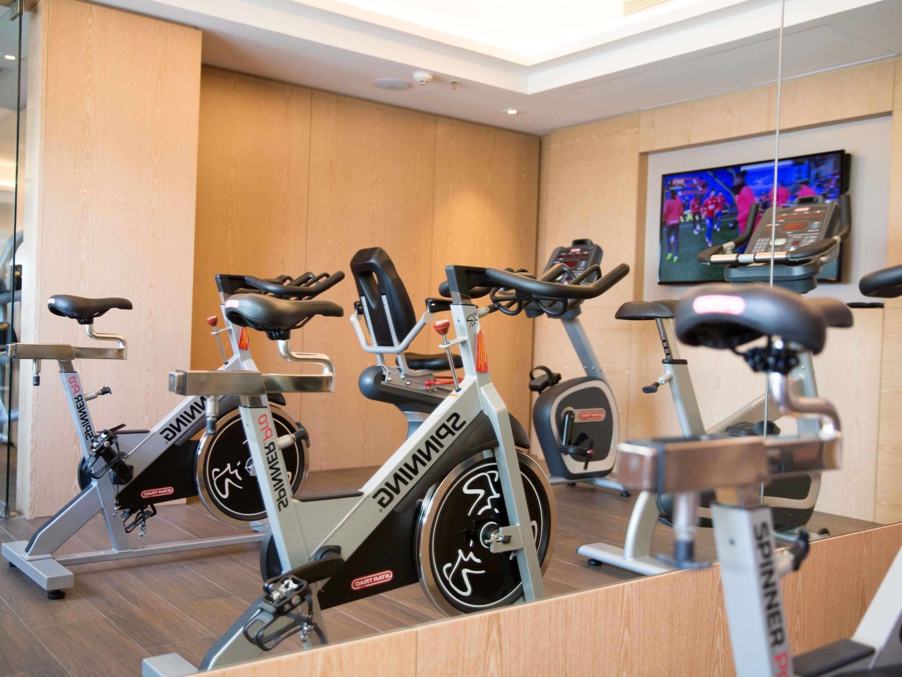 A gym with stationary bikes, a television, and a wooden wall.