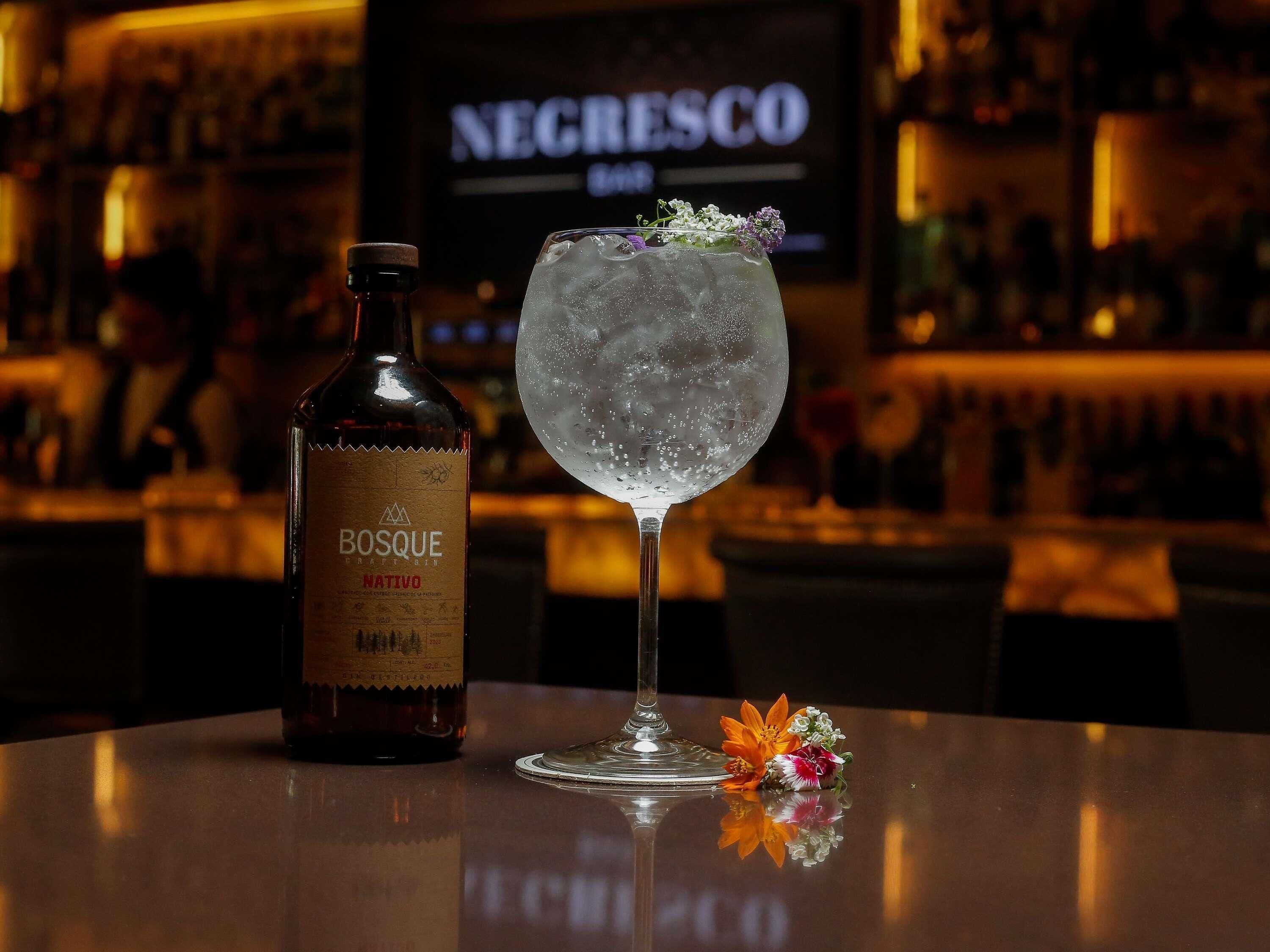 A bottle of Bosque Nativo and a glass with ice and flowers on a bar counter.