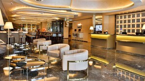 Een hotellobby met een receptiebalie, een barruimte, zitgedeeltes en een kroonluchter.