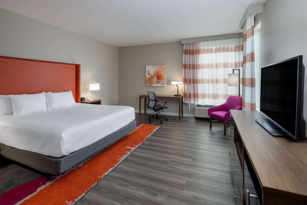 Une chambre d’hôtel avec un grand lit, un bureau avec une chaise, une télévision et une fenêtre avec des rideaux.