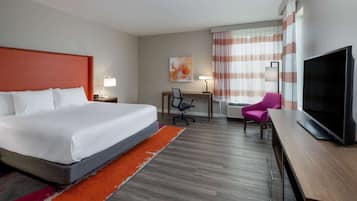 Quarto de hotel com uma cama grande, uma escrivaninha com cadeira, televisão e janela com cortinas.