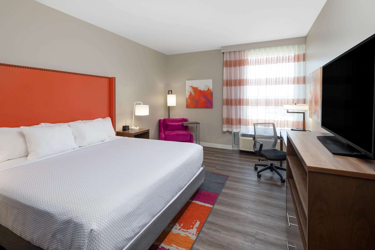Une chambre d’hôtel avec un grand lit, un bureau avec un ordinateur, une télévision et une chaise.