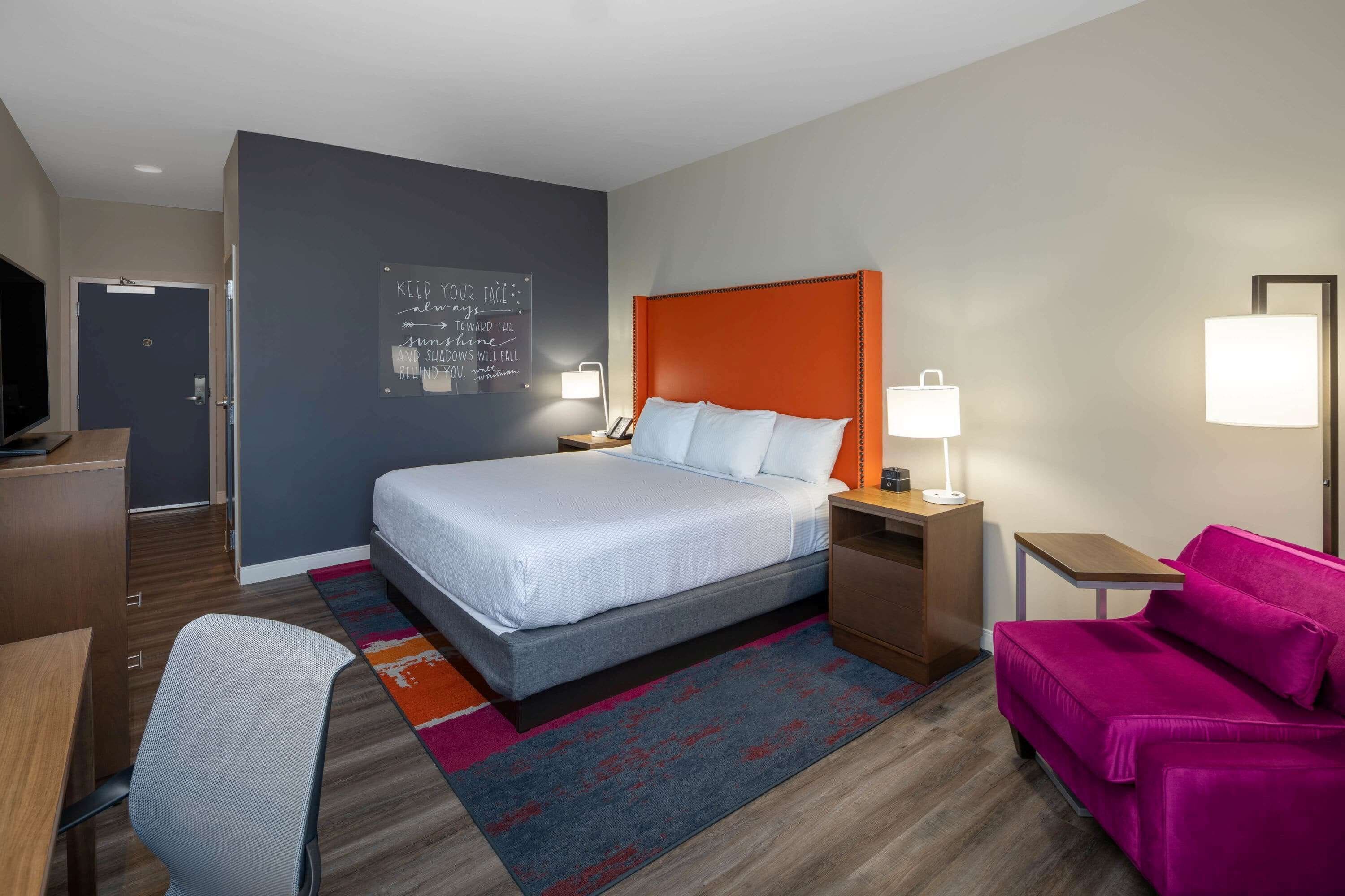 Habitación de hotel con cama, escritorio, silla y sofá rosa.