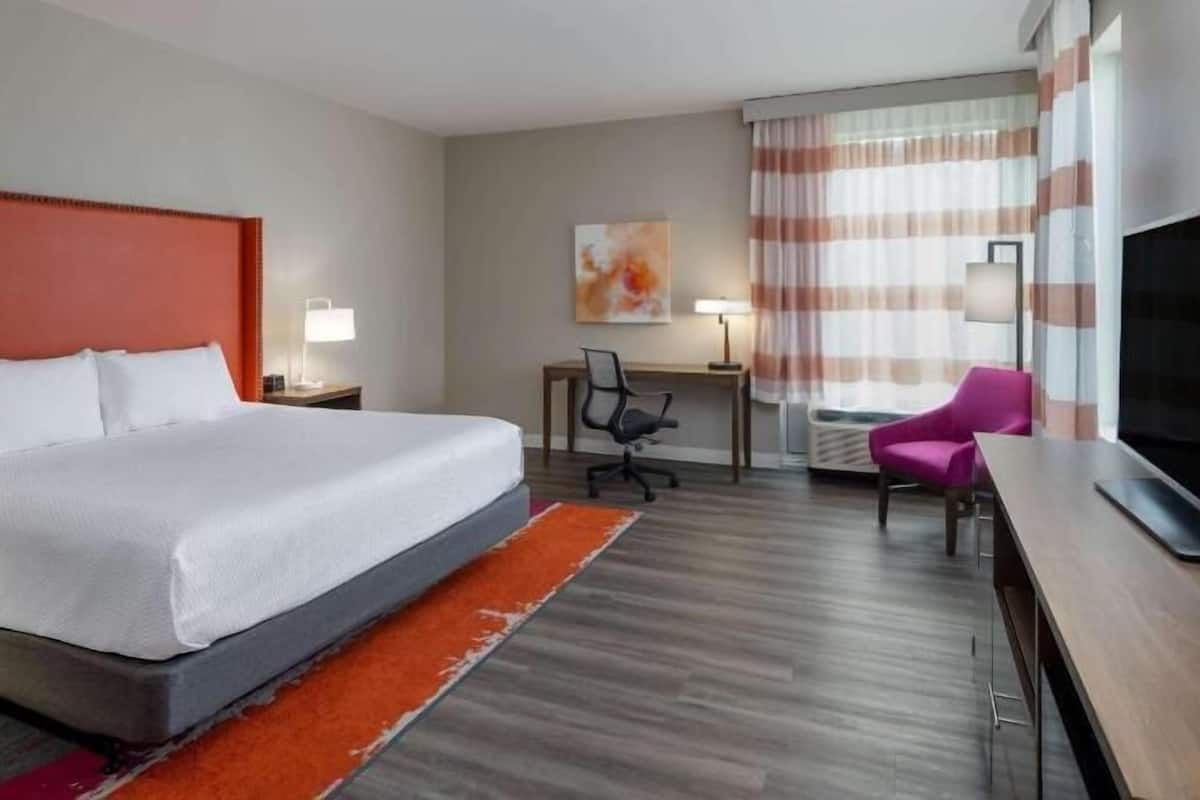 Une chambre d’hôtel équipée d’un lit, d’un bureau, d’une chaise, d’une télévision et d’œuvres d’art accrochées au mur.