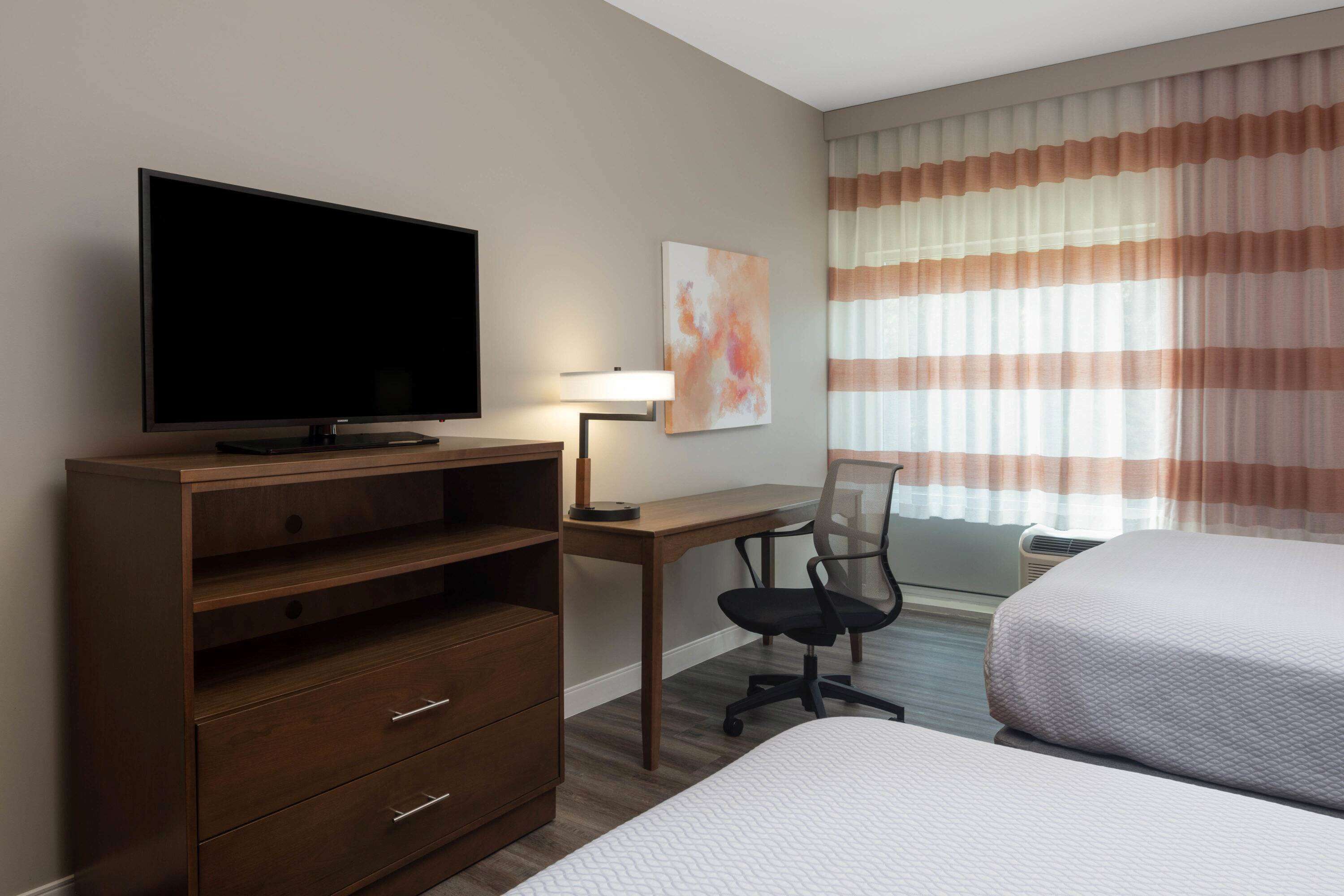 A hotel room with a TV, desk, chair, and two beds.