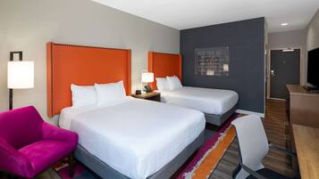 Habitación de hotel con dos camas, un escritorio, un televisor y una pared de acento naranja brillante.
