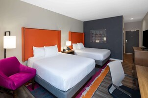 Habitación de hotel con dos camas, un escritorio, un televisor y una pared de acento naranja brillante.
