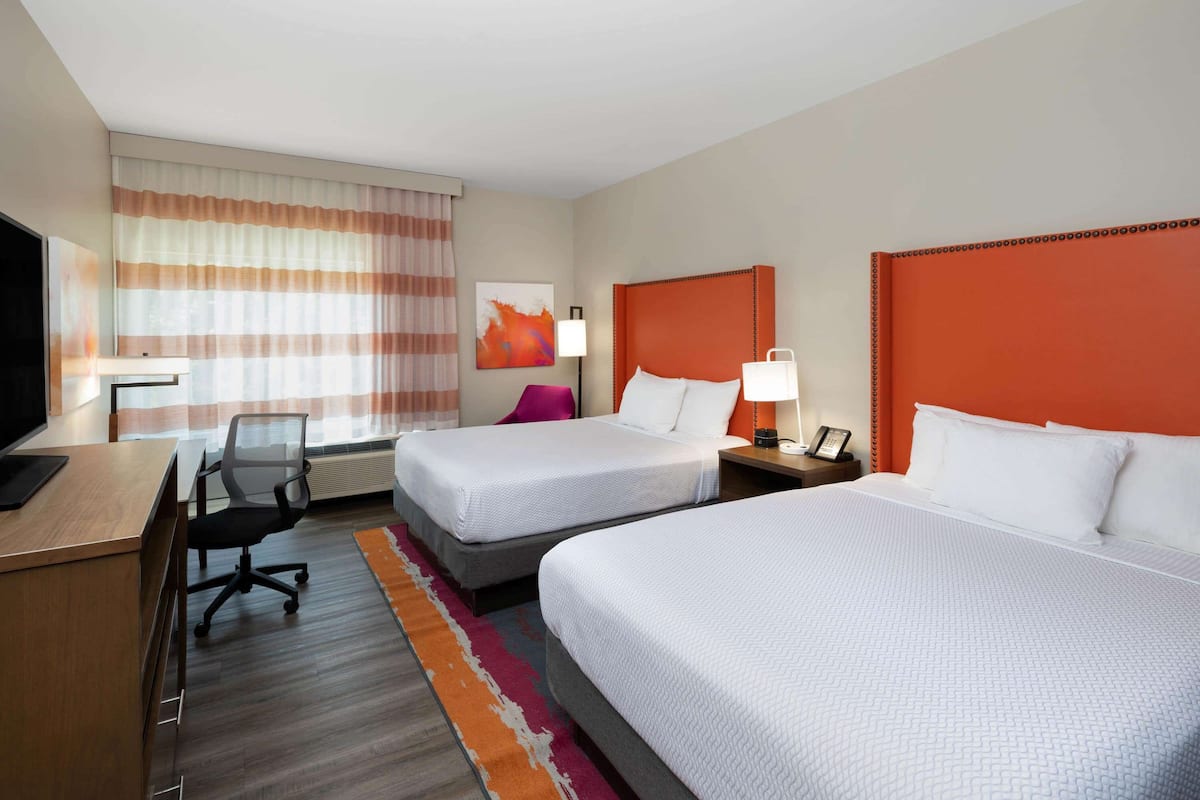 Une chambre d’hôtel avec deux lits, un bureau avec un ordinateur, une chaise, une lampe et un tableau au mur.