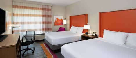 A hotel room with two beds, a desk with a computer, a chair, a lamp, and a painting on the wall.