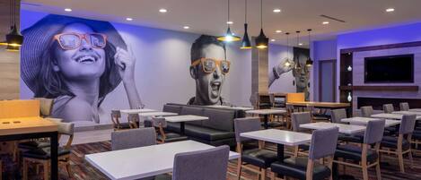 Un restaurant moderne doté d’une grande fresque murale, de nombreuses tables et banquettes, ainsi que d’un écran de télévision fixé au mur.