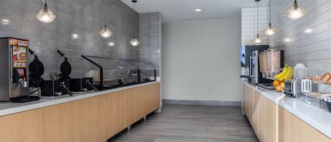 A modern kitchen with a long counter, waffle maker, and a food display.