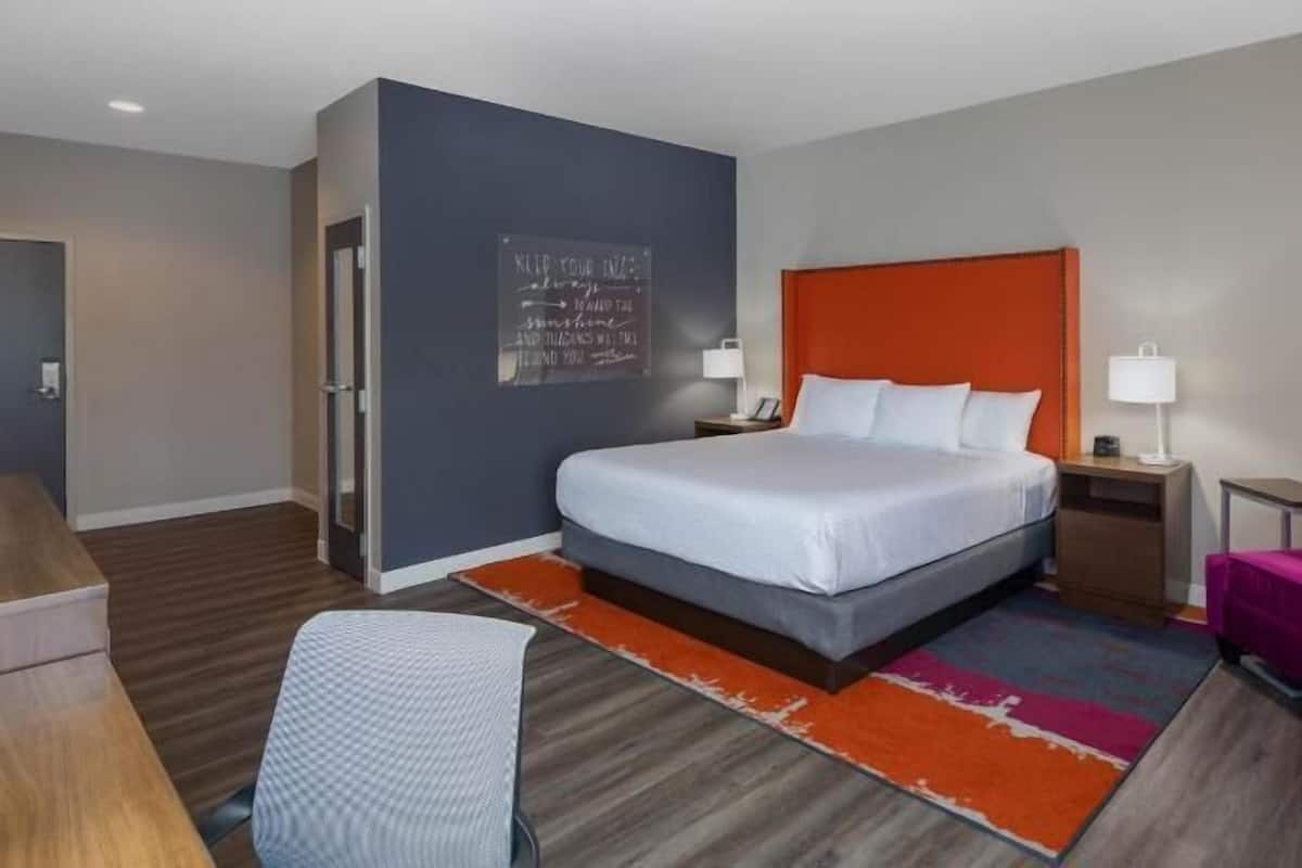 Une chambre d’hôtel comprenant un lit, un bureau, une chaise, une table de chevet et un mur orné d’une citation inspirante.