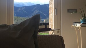 A room with a view of mountains through a door, a chair, a small table with a plant, and a wall-mounted thermostat. - B&B Case Pacifici (Ascoli Piceno)