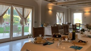 A spacious dining area with a table set for a meal, large windows with curtains, and a view of the outdoors. - B&B Case Pacifici (Ascoli Piceno)