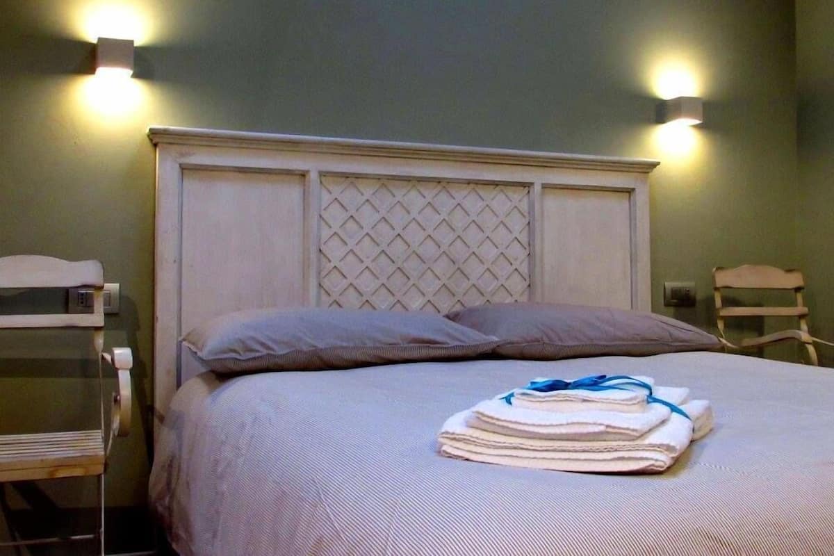 A neatly made bed with a headboard, pillows, and a stack of folded towels.
