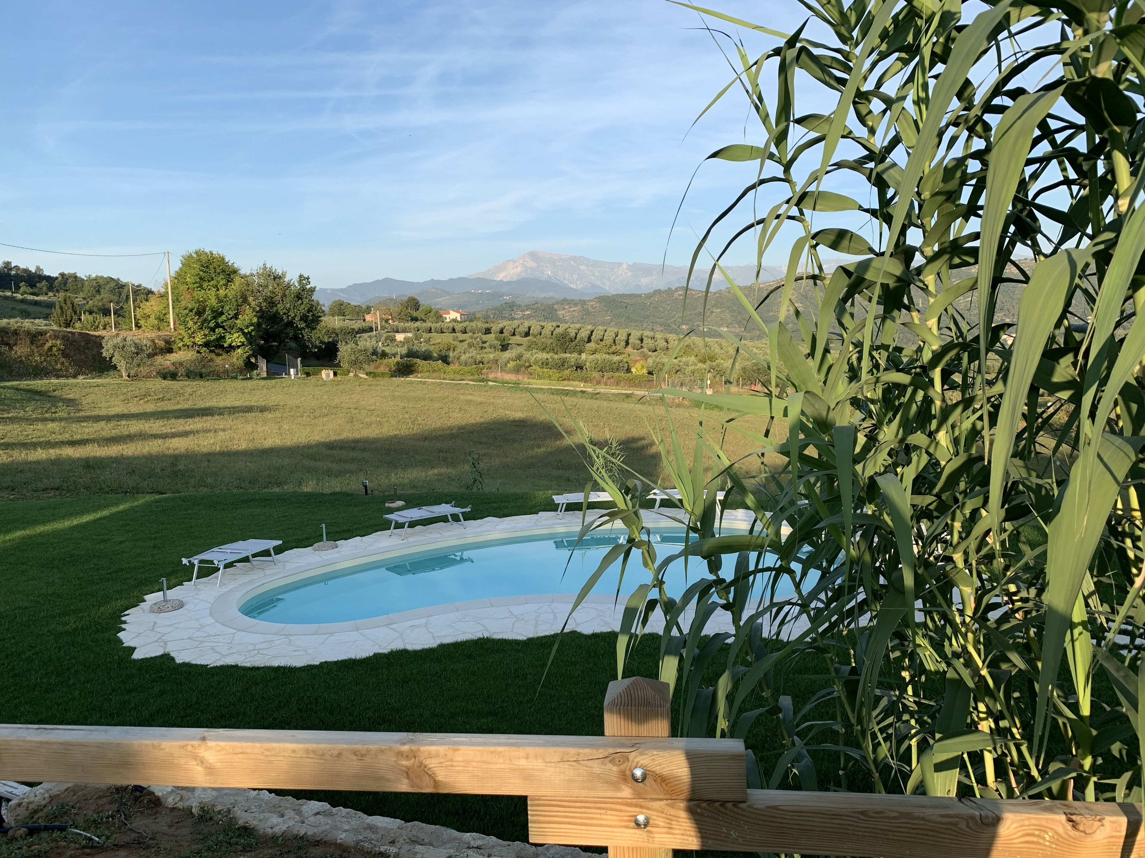 A swimming pool with a surrounding deck, a wooden fence, and a view of a mountainous landscape.