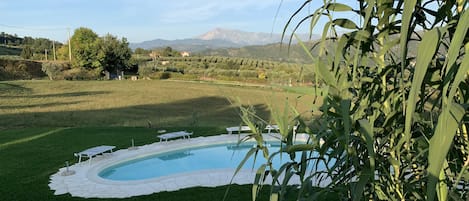 A swimming pool with a surrounding deck, a wooden fence, and a view of a mountainous landscape.