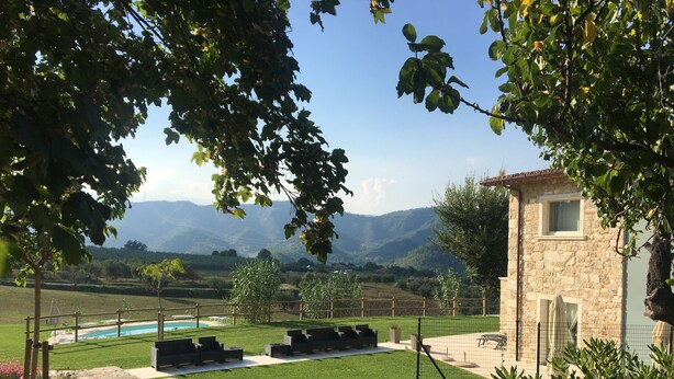 A stone building with a pool and outdoor seating area, surrounded by greenery and mountains in the background. - B&B Case Pacifici (Ascoli Piceno)