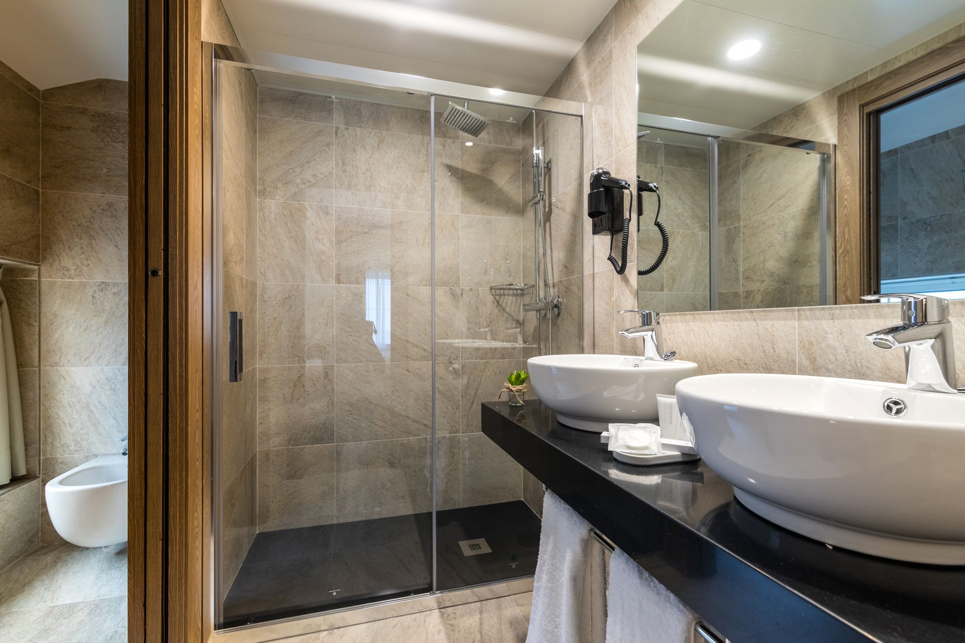 Un baño moderno con ducha de vidrio, dos lavamanos y un espejo grande.