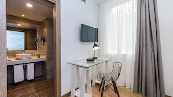 A modern bathroom with a large mirror, a sink, and a shower. There is a glass table with a chair and a TV mounted on the wall.