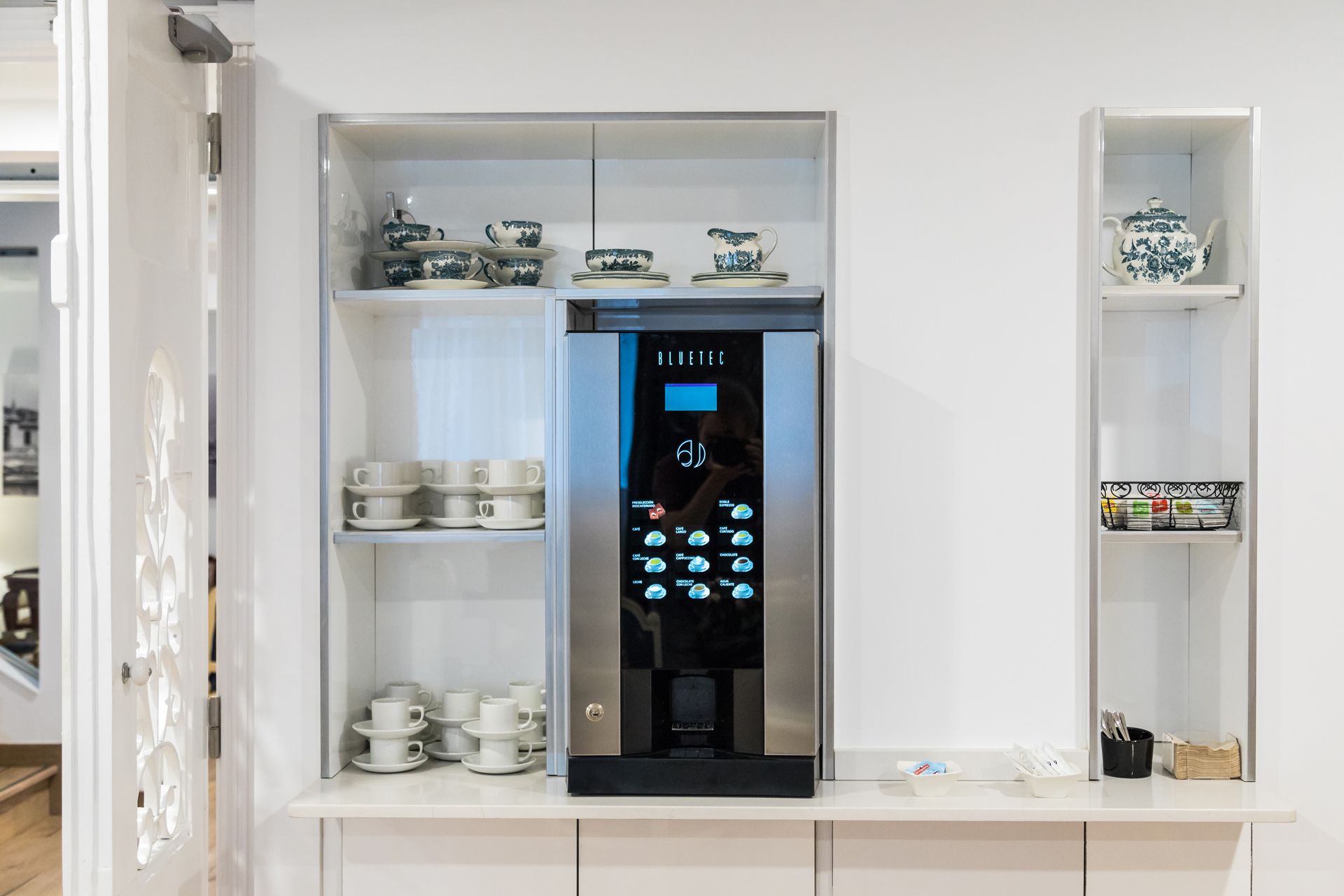 Màquina de cafè amb pantalla digital i una selecció de tasses i platets a prestatgeries.