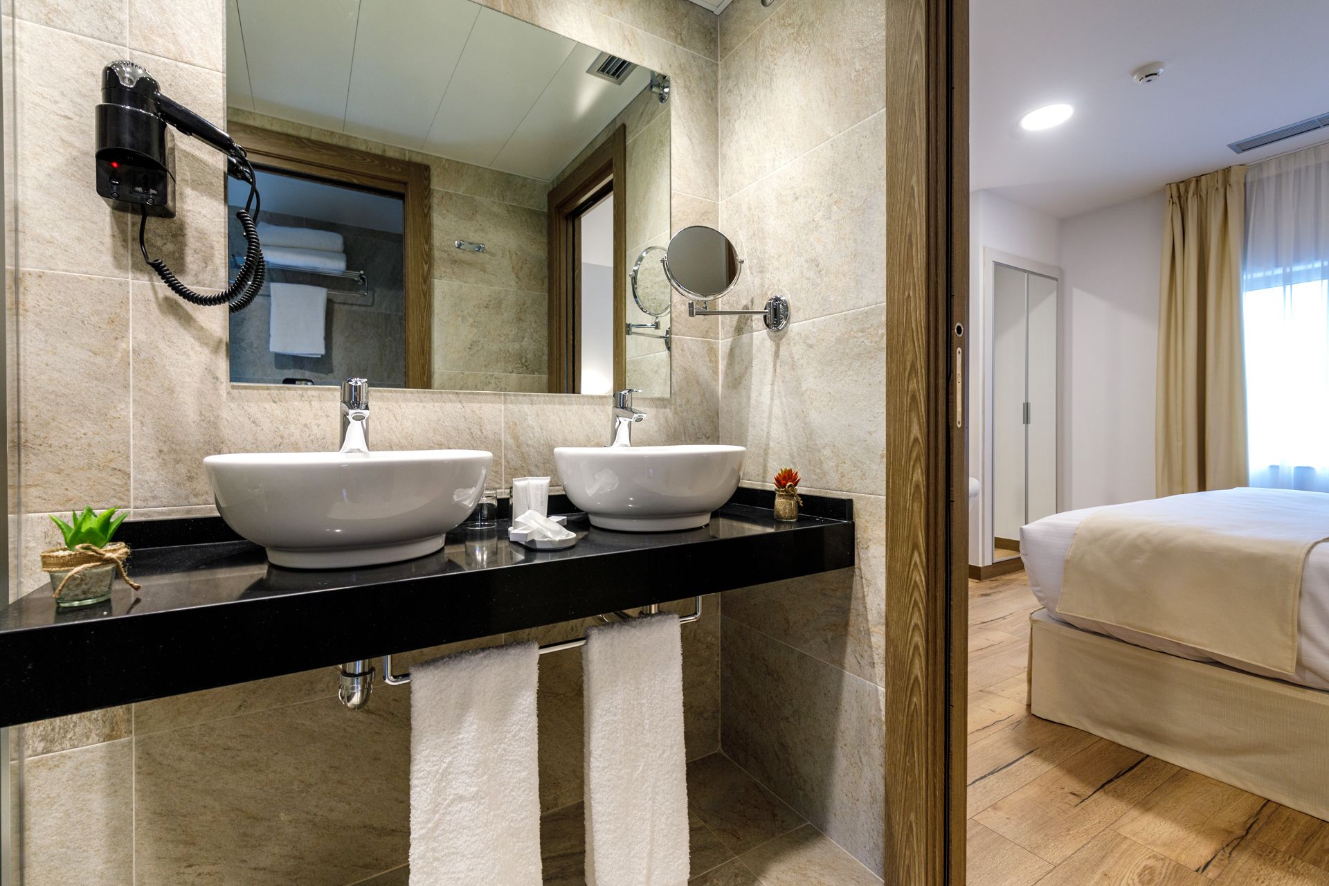 A hotel bathroom with two sinks, a hairdryer, and a mirror.