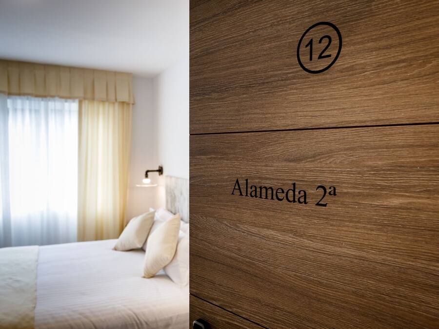 A hotel room with a bed, a nightstand, and a wooden wall with the number 12 and the name "Alameda 2a".