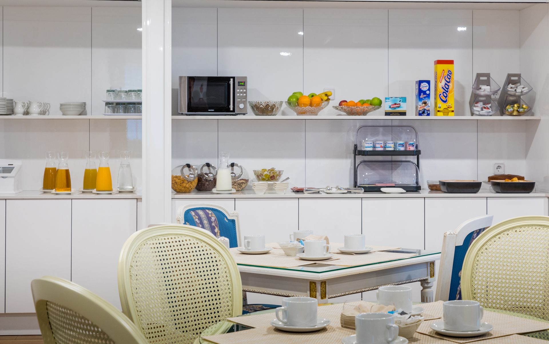 Cocina moderna con armarios blancos, un microondas, una cafetera y diversos alimentos en estantes.