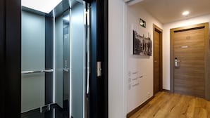 A hotel lobby with a wooden floor, a wooden door labeled '12', and a wall with numbered signs indicating room locations. - Suite Home Pinares (Santander)