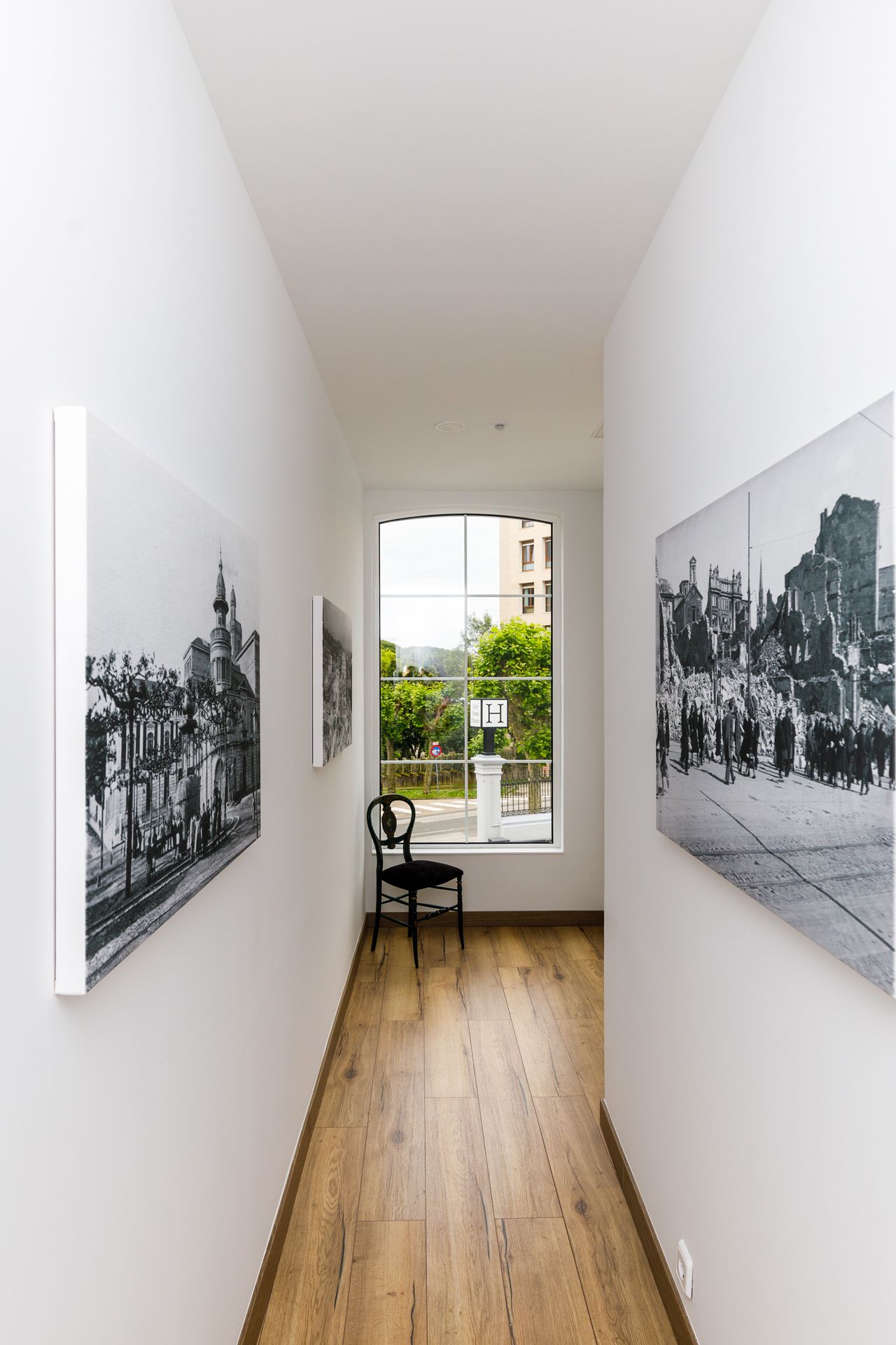 A hallway with wooden flooring, a chair, and two black and white photographs on the walls.