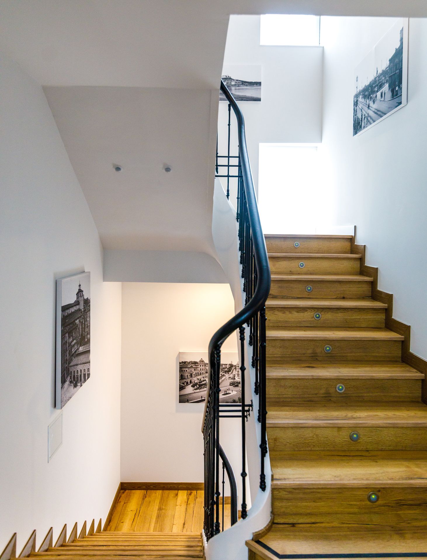 A wooden staircase with black railings, white walls, and two black-and-white photographs.