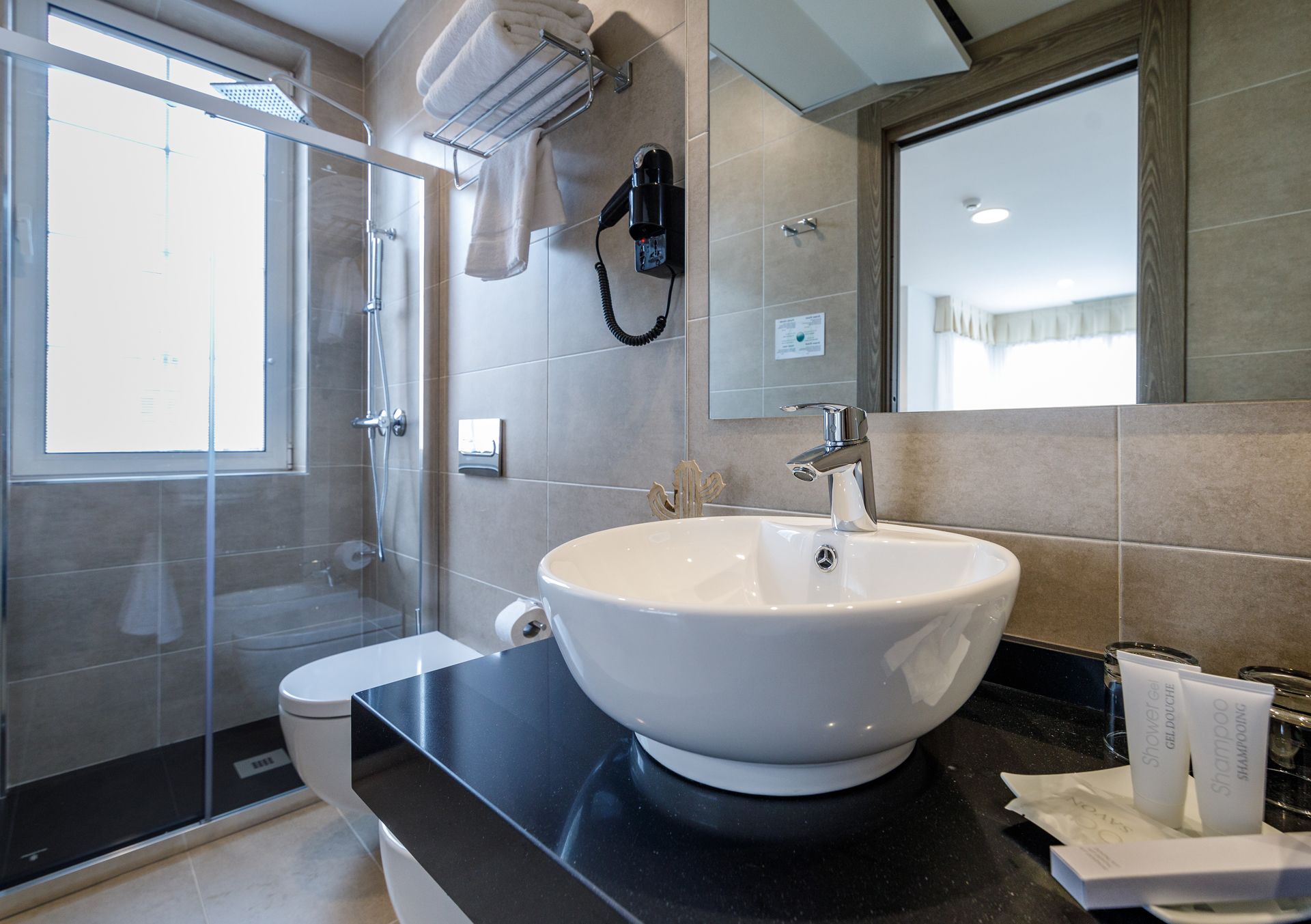 Un baño moderno con un lavamanos grande de color blanco, cabina de ducha con mampara de vidrio y encimera negra.
