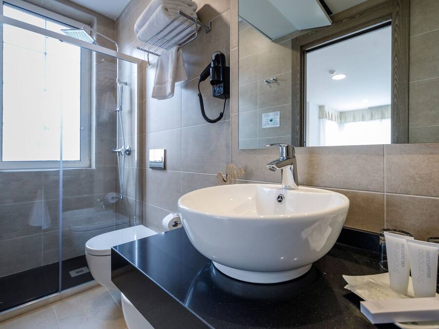 Un baño moderno con un lavamanos grande de color blanco, cabina de ducha con mampara de vidrio y encimera negra.