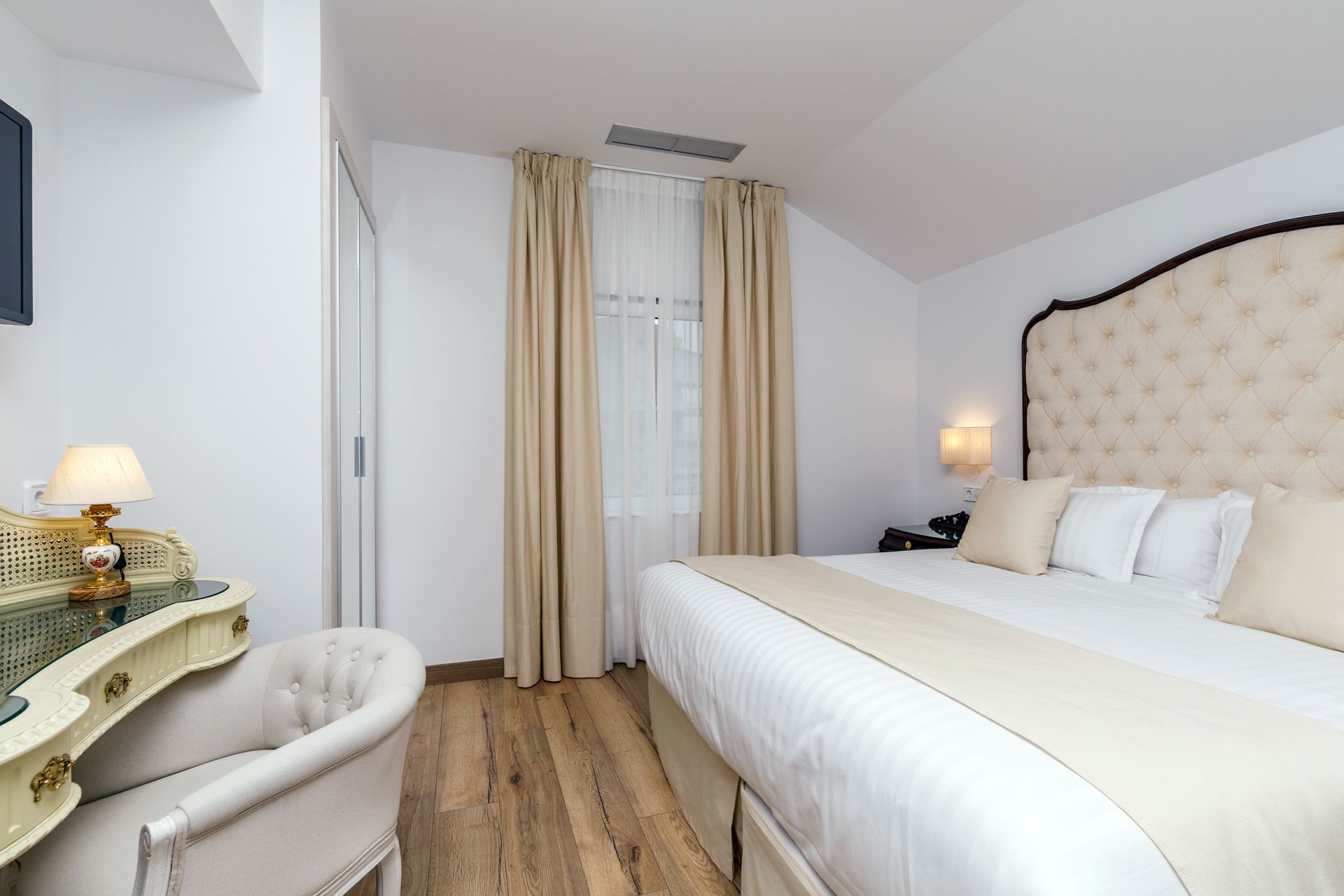 Ein Hotelzimmer mit einem großen Bett, einem Nachttisch mit Lampe, einem Sessel und einem Fenster mit Vorhängen.