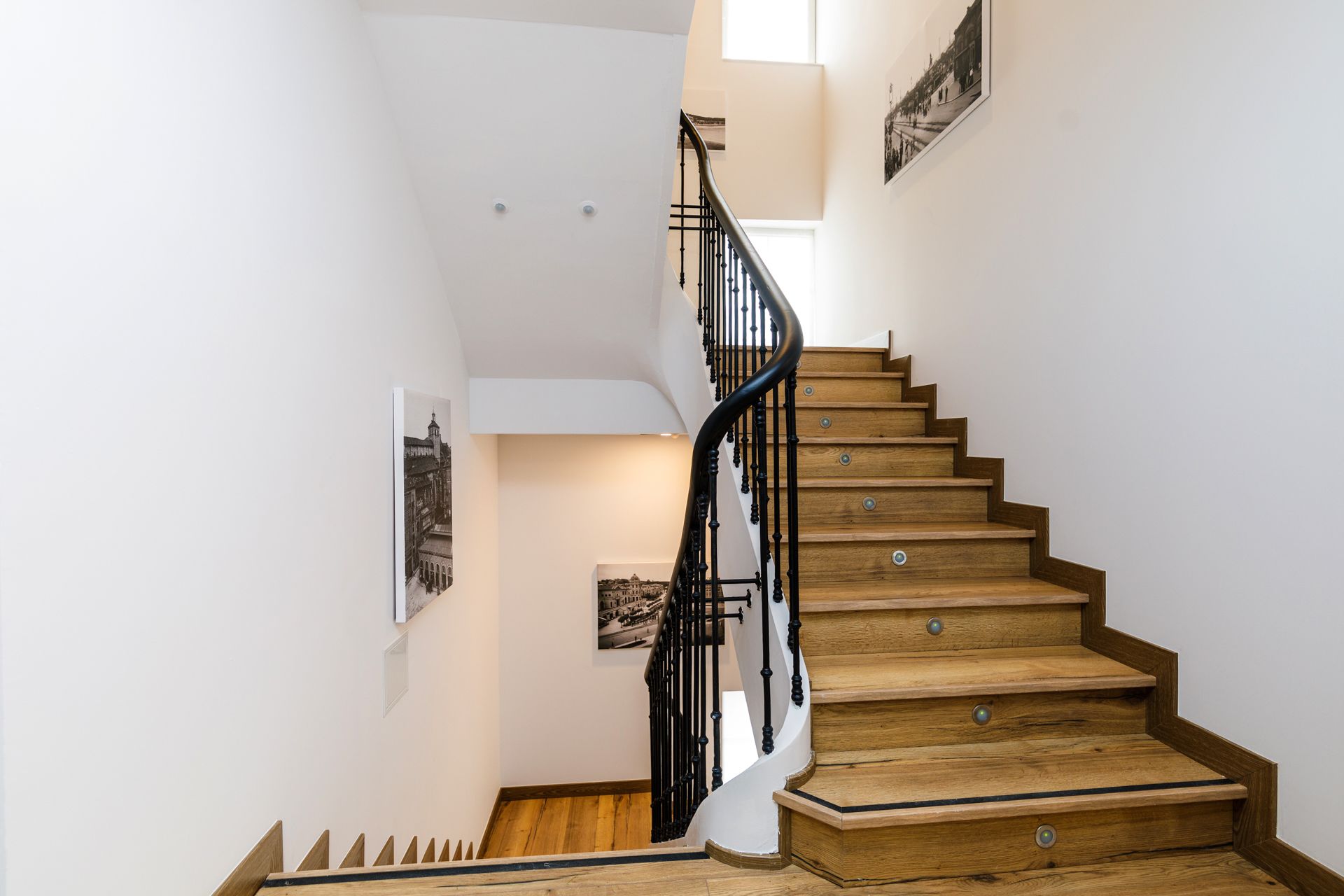 A wooden staircase with black railings and multiple photographs on the walls.